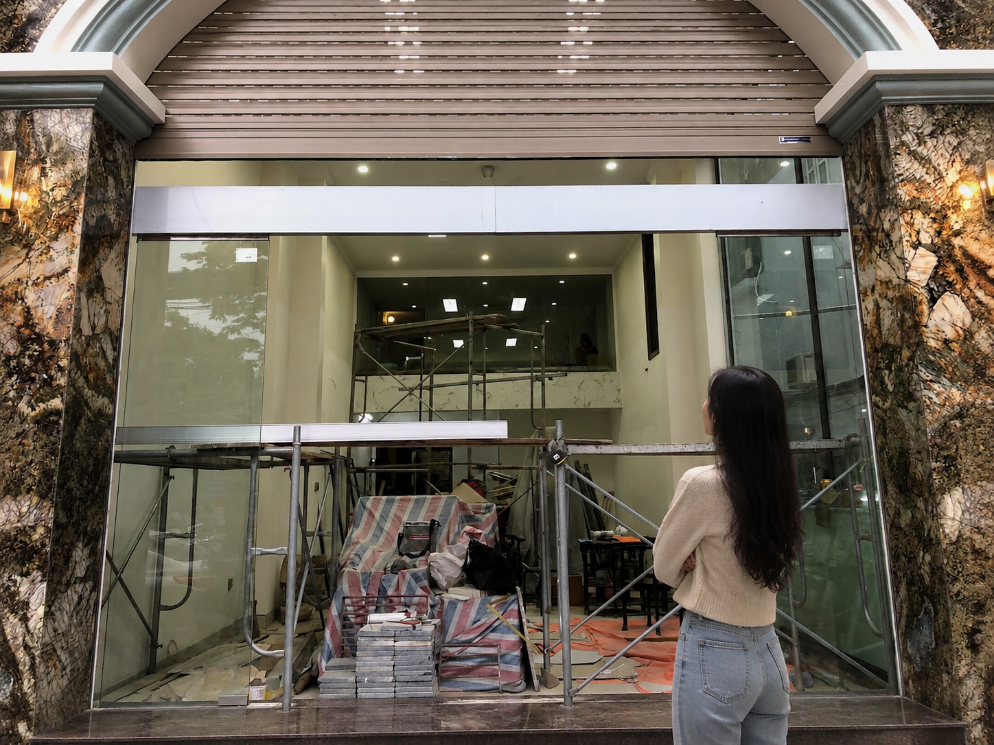 Cửa kính mặt tiền nhà phố đang thi công nội thất, giàn giáo và vật liệu xây dựng bày phía trong